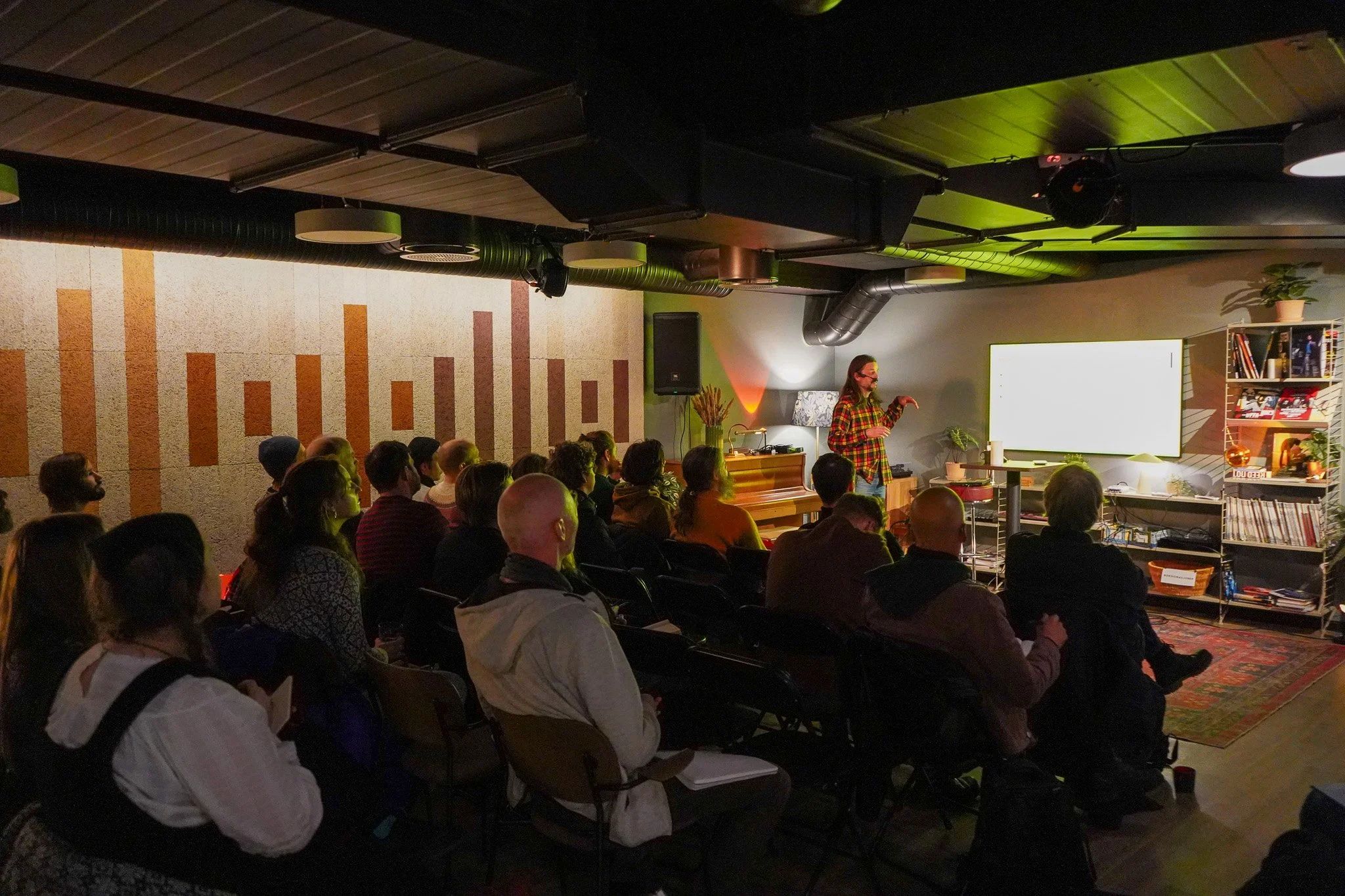 Fullsatt seminar i fellesarealet på Øveriet, med en foredragsholder foran et lerret.